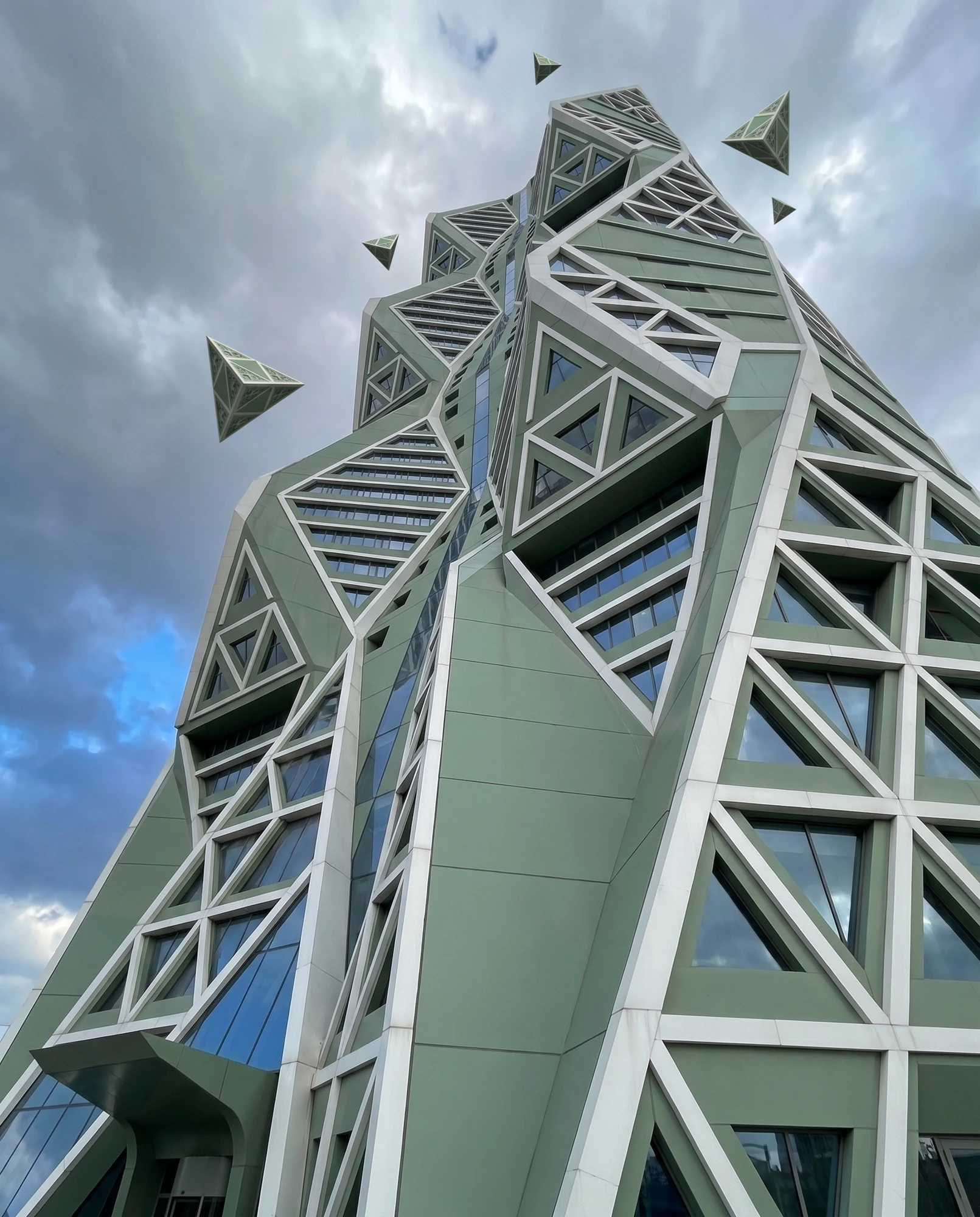 A green geometric tower and floating triangular forms against the sky.