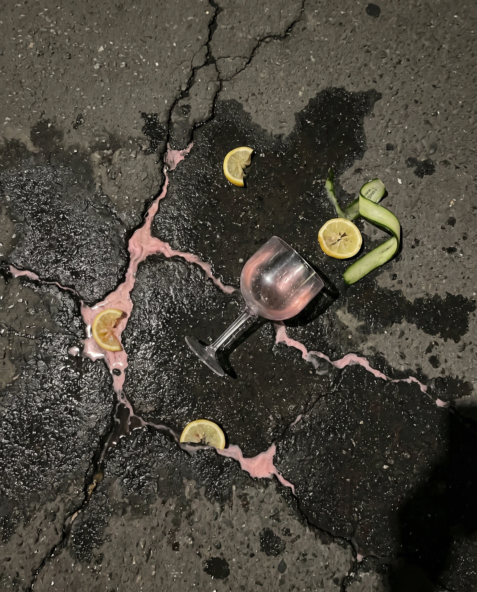 A spilled pink drink, citrus slices and a glass on the pavement.